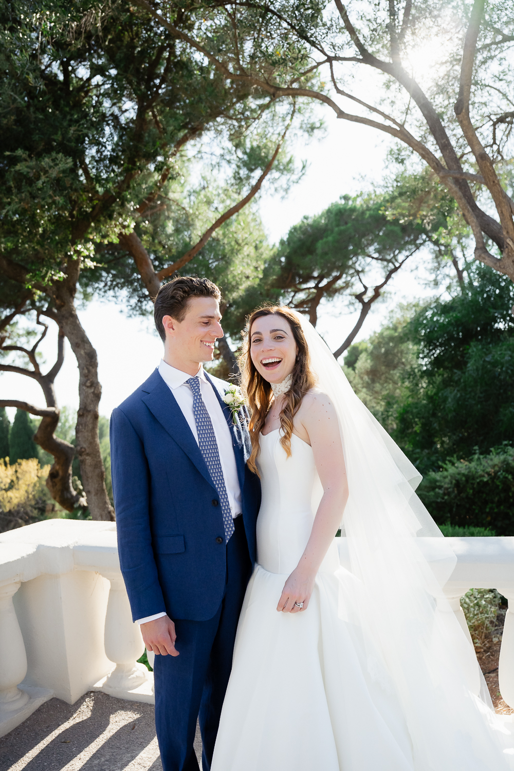 A joyful couple stands beneath Mediterranean pines as sunlight filters through the trees, moments after their wedding ceremony in Provence.
