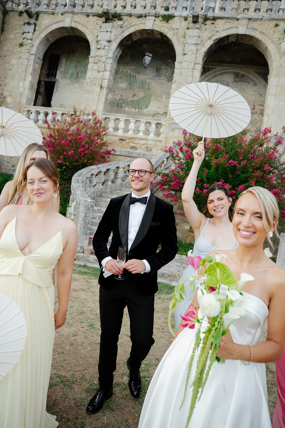 The bride celebrate with bridesmaids and friends in front of Château de Poudenas, where white parasols, colourful summer flowers and joyful expressions bring the cocktail hour to life.